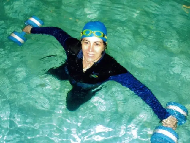 A swimmer in a black wetsuit floating on foam dumbbells in aqua water