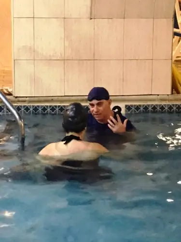 An instructor beside a student at the tiled pool edge