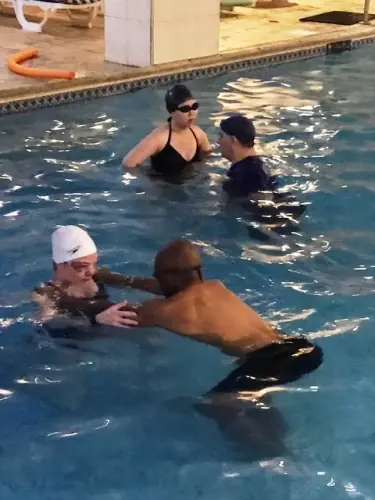 Two lessons under way at the pool edge with an orange noodle on the deck